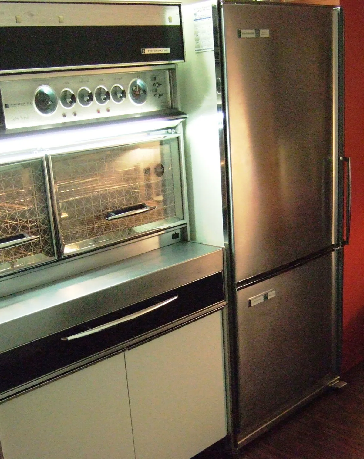 A 1963 Frigidaire Imperial bottom freezer refrigerator in brushed steel, built into a kitchen beside a wall oven.