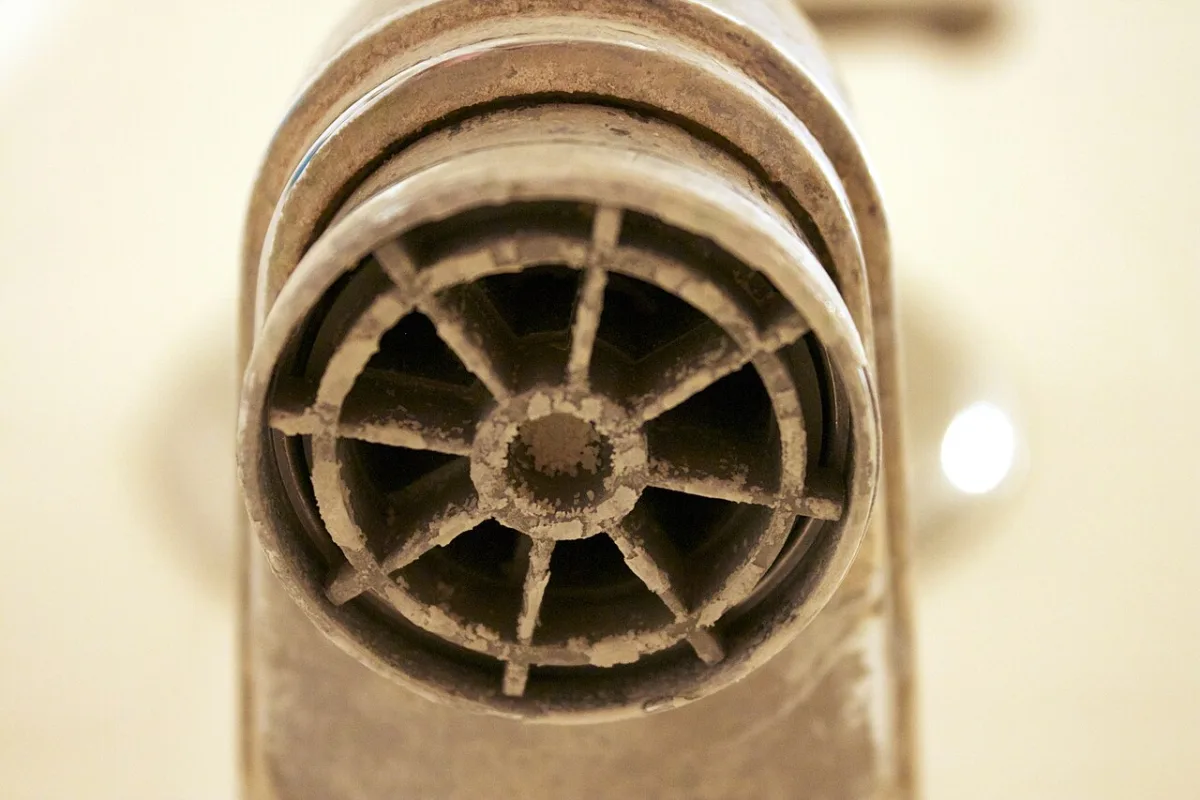 Close up of a tub faucet spout crusted with white and tan mineral scale from hard water.