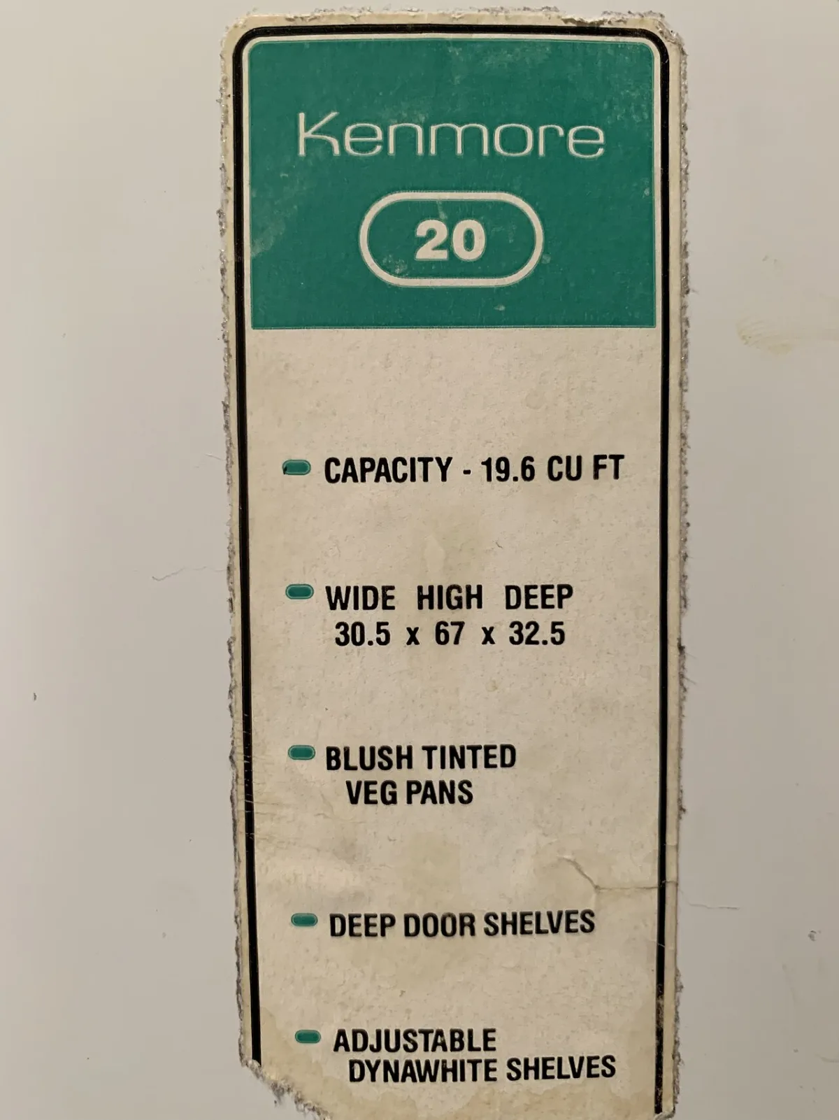 A worn green and white Kenmore 20 label on a refrigerator listing capacity 19.6 cubic feet and its size and shelf features.