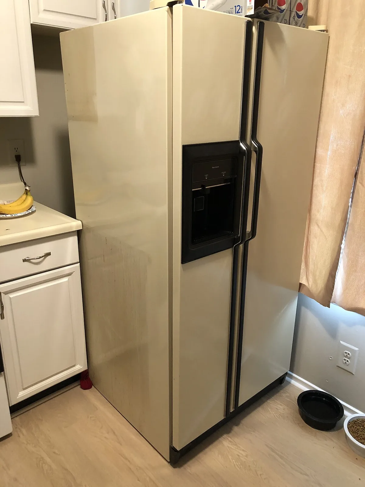An almond colored Kenmore side by side refrigerator with an ice and water dispenser, in a home kitchen.