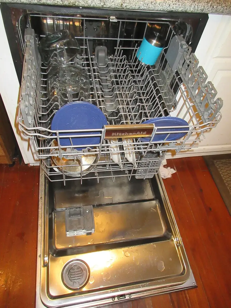 Open built-in dishwasher with the racks pulled out and a round filter cover visible in the floor of the tub