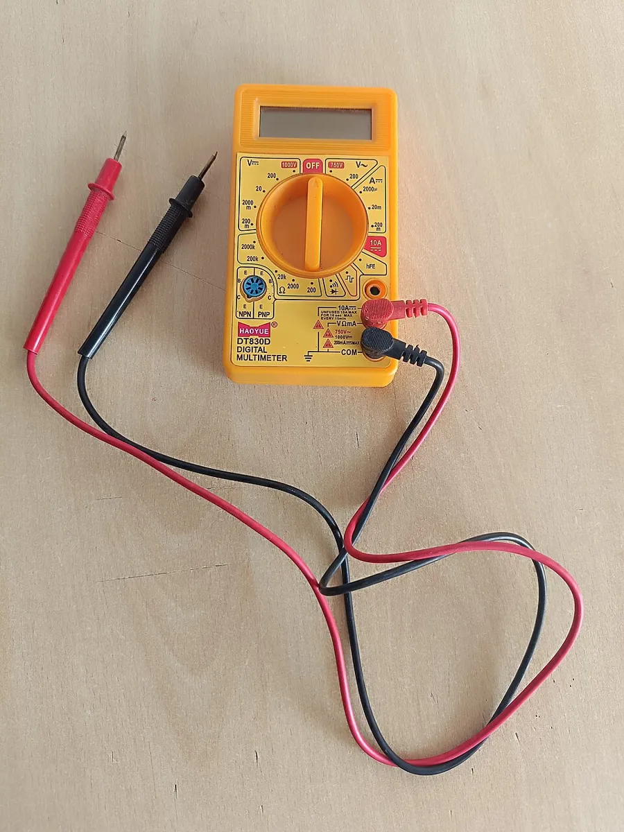 A yellow digital multimeter with red and black test leads lying on a wooden table