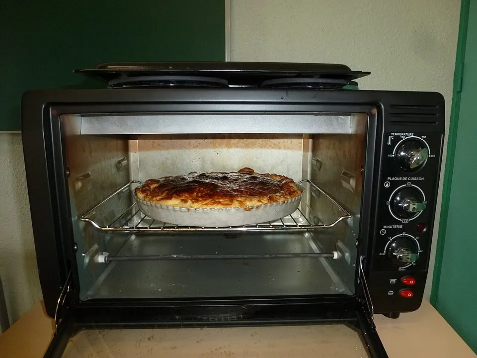 Open countertop electric oven with a pie on the rack and a rod shaped heating element along the floor of the oven