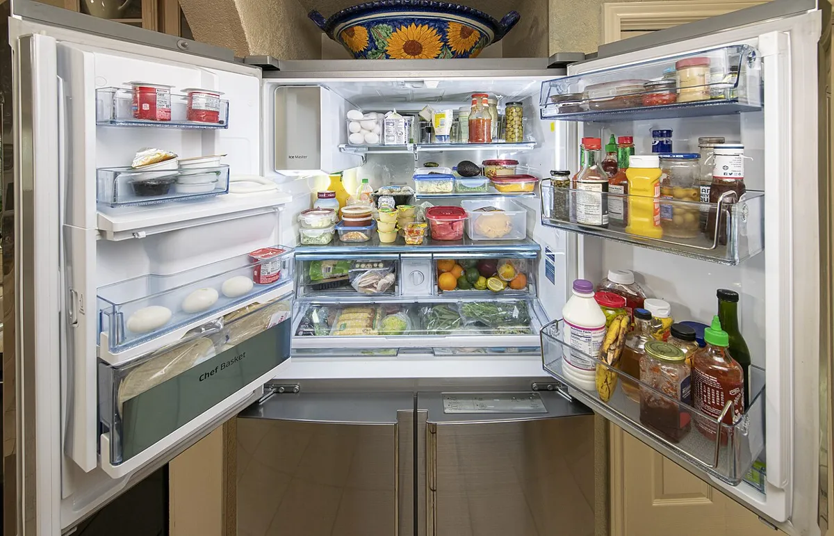 A French door refrigerator with both doors open, shelves and door bins full of food